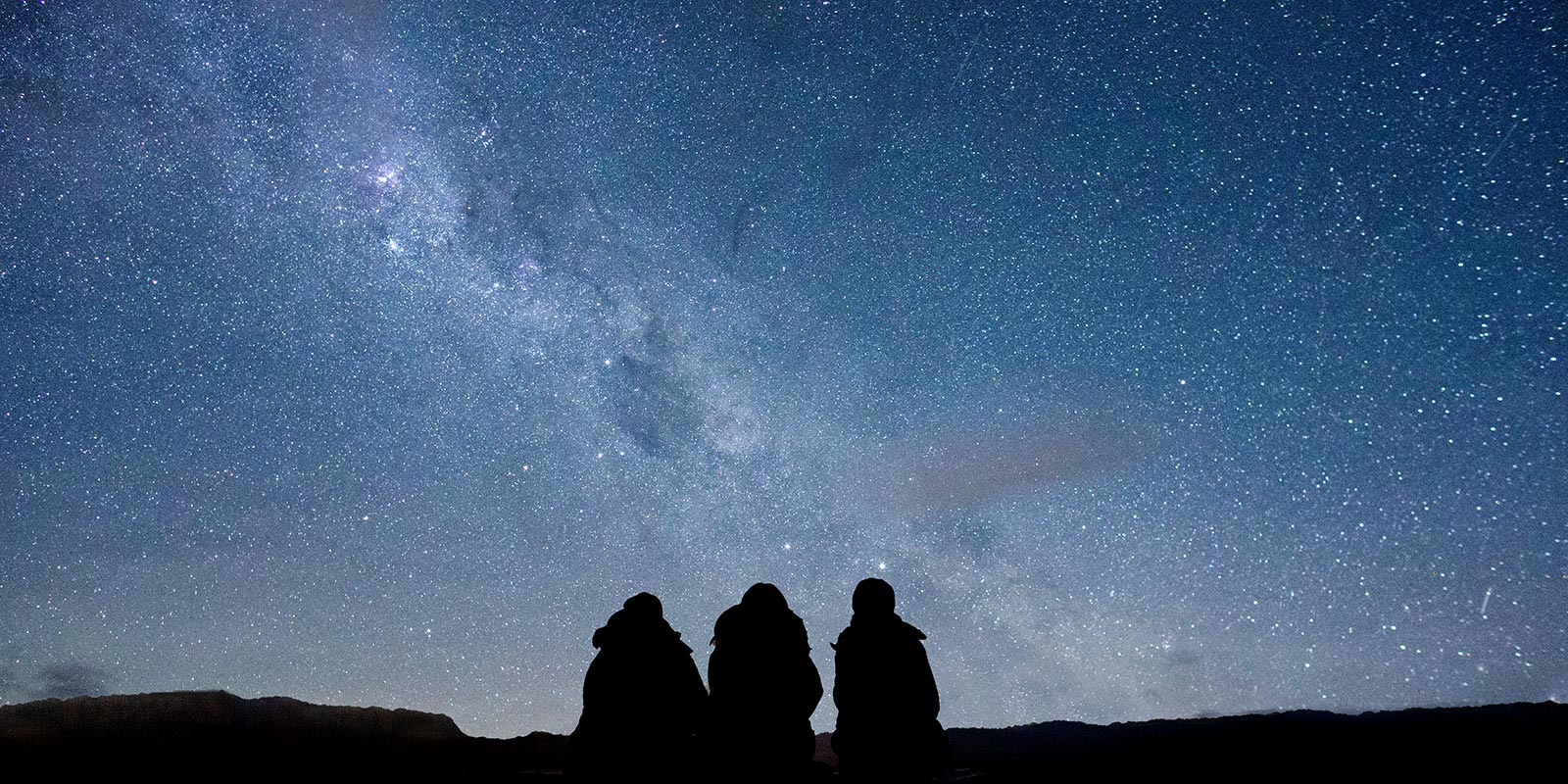 Three figures silhouetted against a star-filled sky at Dark Sky Project, Lake Tekapo