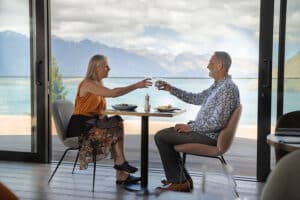 Middle-aged couple clinking wine glasses at a Queenstown restaurant with panoramic views of Lake Wakatipu