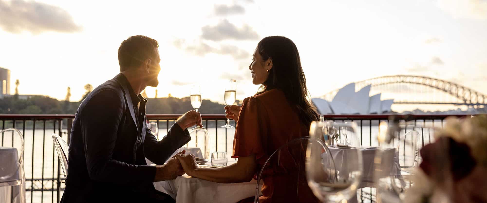 Couple dining at Mrs Macqueries Chair in Sydney, drinking wine with views of the harbour