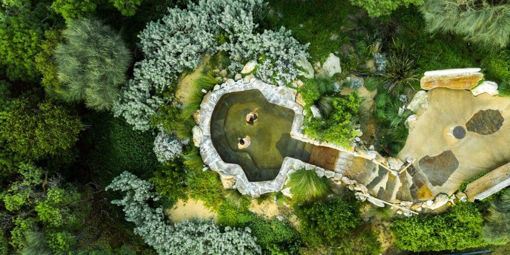 Aerial view of a thermal pool surrounded by lush greenery at Peninsula Hot Springs