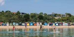 Stand up paddleboarding in the ocean near colorful bathing houses on the beach